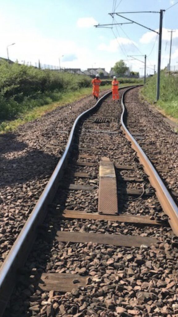 Very bent rail on a hot day with two track workers in the background.