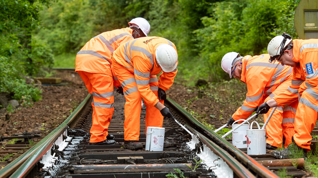 four engineers on a single line of railway track painting the rails white to reduce heat.