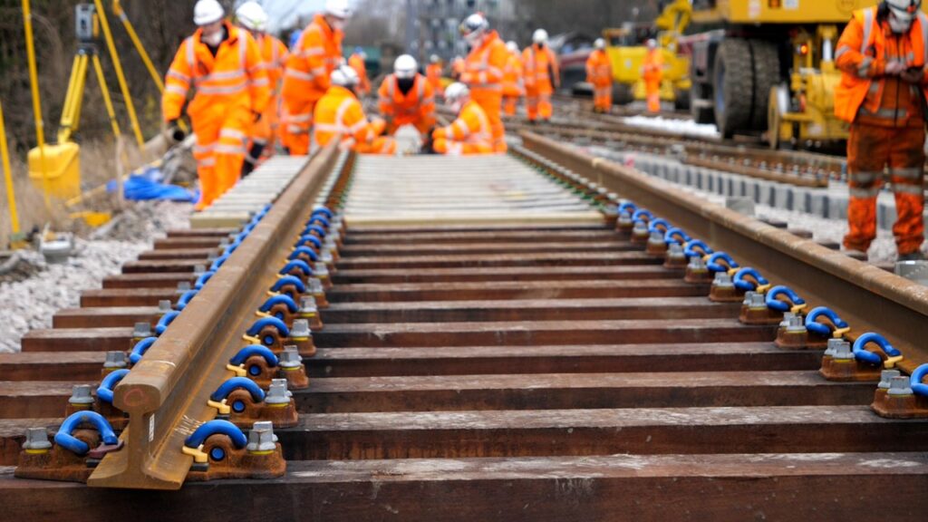 new track close up with engineers in orange PPE working in the background