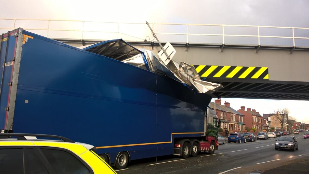 Photograph of a blue HGV hitting a railway bridge and damaging its roof.