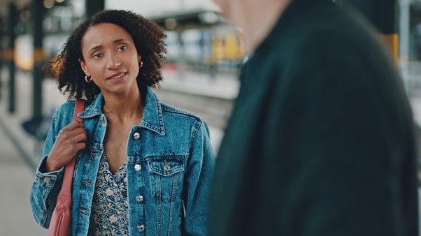 A woman approaches a person on a railway station platform.