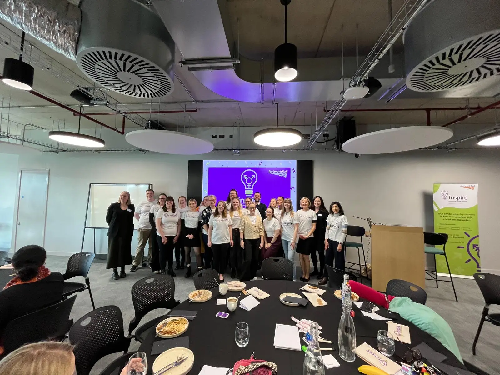 Inspire's leadership team - with executive sponsor Ellie Burrows on the far left - at Inspire's 2025 conference. The team stands in a large function room in front of a screen with a purple graphic.