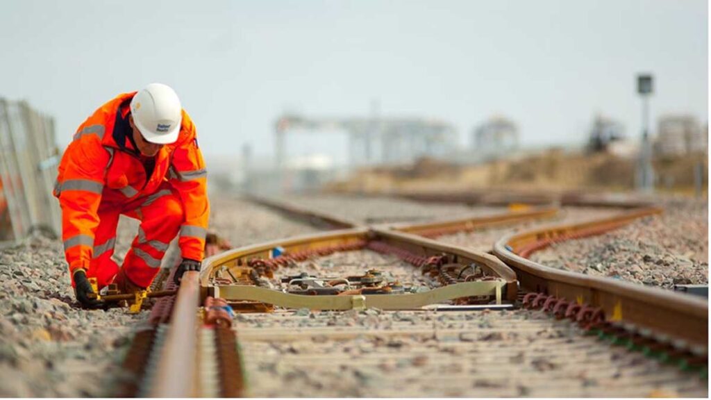 A rail worker working on a piece of track on a sunny day.