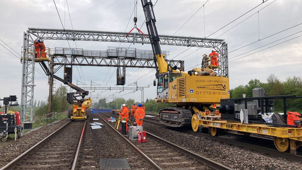 Landscape image of rail workers on the tracks working on the gantry.