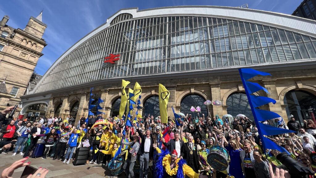 Eurovision crowds with banners outside Liverpool Lime Street.