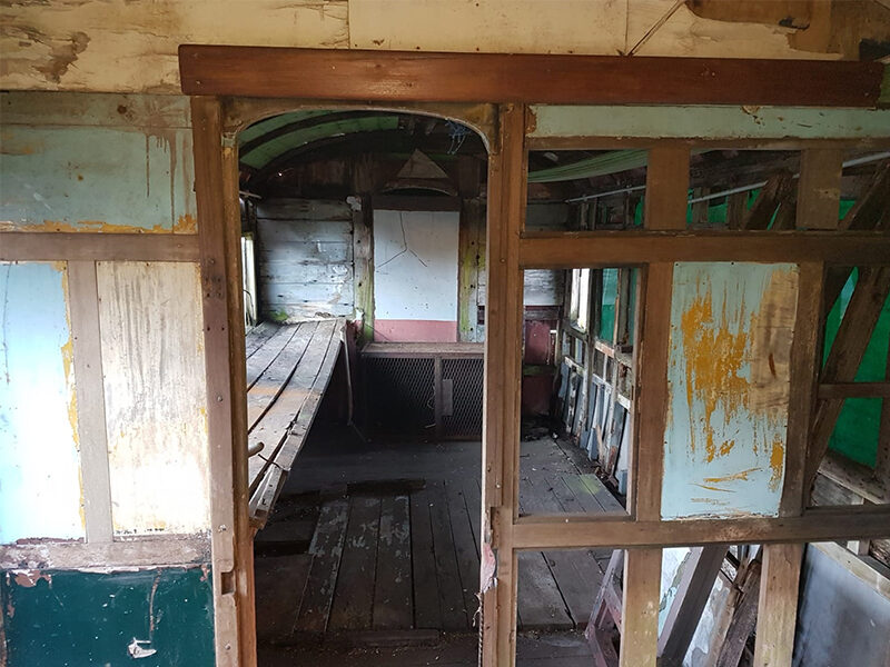 Interior of an old, abandoned first class train carriage of a Titanic boat train with peeling paint and visible wooden frame structure.