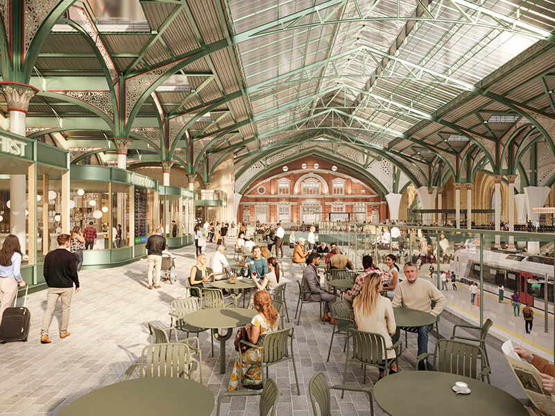 Artistic recreation of the upgraded bustling balcony of London Liverpool Street station with arched green metal ceilings, intricate columns, numerous visitors seated at café tables, and shops lining the perimeter.